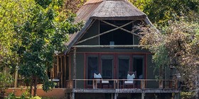 Thatched tented suite on stilts at the water's edge surrounded by riverine woodland at Royal Zambezi Lodge, Lower Zambezi, Zambia