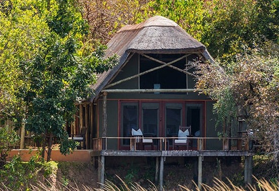 Thatched tented suite on stilts at the water's edge surrounded by riverine woodland at Royal Zambezi Lodge, Lower Zambezi, Zambia