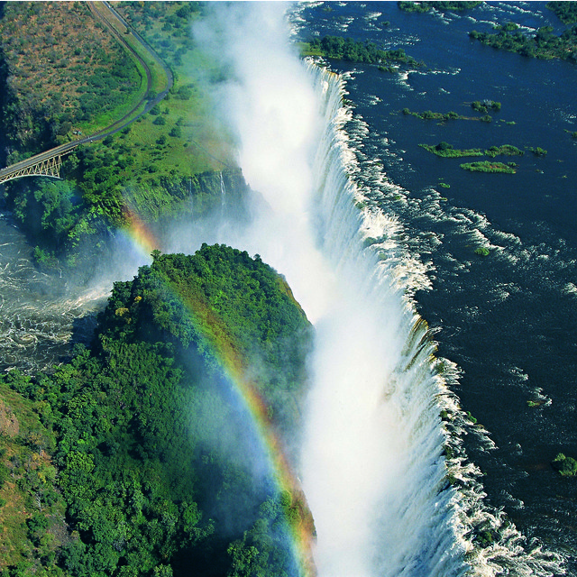 Aerial view of Victoria Falls with a vivid rainbow over the Zambezi River gorge and historic bridge, Zimbabwe