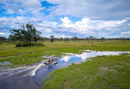 Aerial view of a motorboat speeding along a river channel through lush green floodplains of the Okavango Delta, Botswana