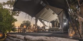 Safari tent exterior at dusk with lanterns glowing on a log deck overlooking the Okavango Delta at Kweene Camp, Botswana