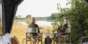 Two guests seated in camp chairs looking out over the Okavango Delta floodplains from inside their safari tent at Kweene Camp, Botswana