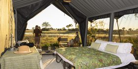 Safari tent interior at Magwegwe Camp with guests photographing sunrise over the Okavango Delta floodplains, Botswana