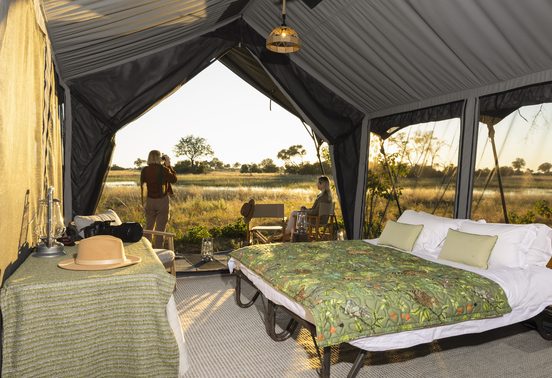 Safari tent interior at Magwegwe Camp with guests photographing sunrise over the Okavango Delta floodplains, Botswana