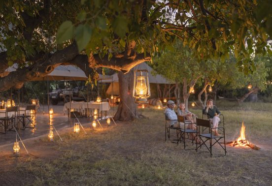Guests gathered around a campfire beneath lantern-lit trees at Magwegwe Camp, Okavango Delta, Botswana