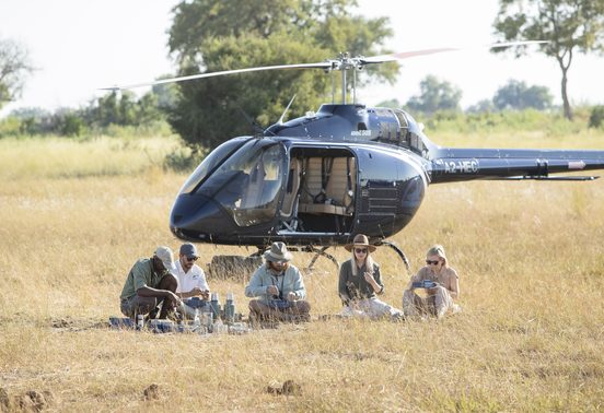 Guests enjoying a bush breakfast on the grass beside a helicopter during a scenic heli flight over the Okavango Delta, Botswana