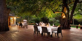 Candlelit outdoor dining tables set beneath ancient trees at Thamo Telele, Okavango Delta, Botswana