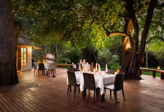 Candlelit outdoor dining tables set beneath ancient trees at Thamo Telele, Okavango Delta, Botswana