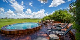 Round plunge pool on a timber deck with sun loungers overlooking green floodplains under a blue sky at Karangoma, Okavango Delta, Botswana