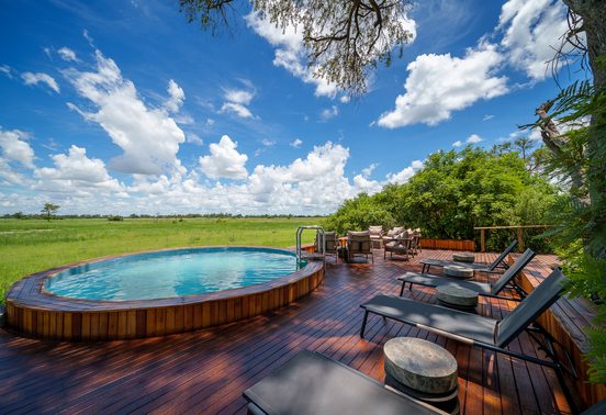 Round plunge pool on a timber deck with sun loungers overlooking green floodplains under a blue sky at Karangoma, Okavango Delta, Botswana