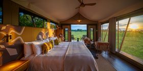 Luxurious safari tent interior with bold patterned headboard and king bed looking out over a sunset floodplain at Karangoma, Okavango Delta, Botswana